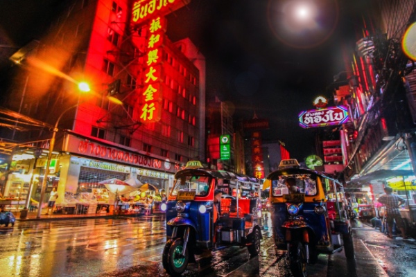 Tuk-tuks on a vibrant, neon-lit street at night in Bangkok.