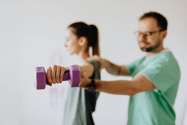 An intern helping out a patient with a short barbell.