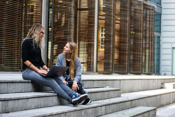 pexels-buro-millennial-1438084 (1) Two women sitting on the stairs, one of them holding a laptop.