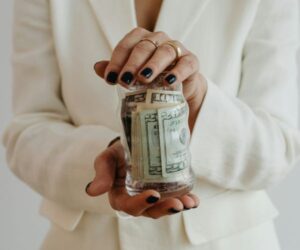 a woman in a white suit holding a jar of money