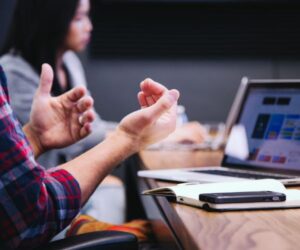 Person gesturing while discussing something in front of a laptop during a meeting