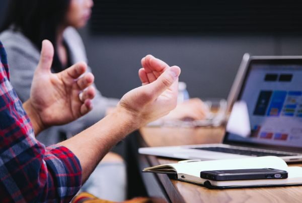 Person gesturing while discussing something in front of a laptop during a meeting
