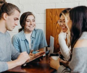 four young people talking and smiling while working together at a table