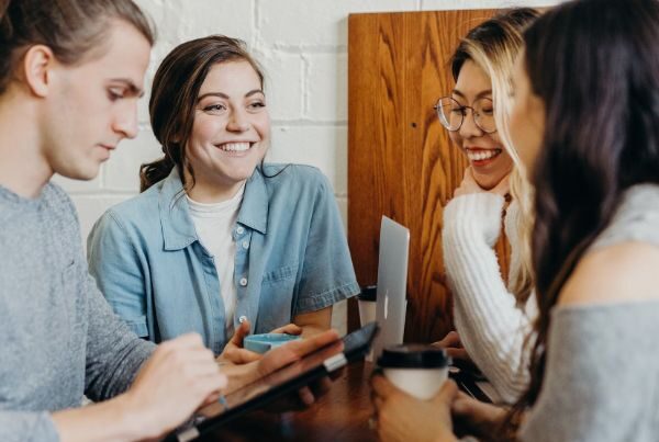 four young people talking and smiling while working together at a table