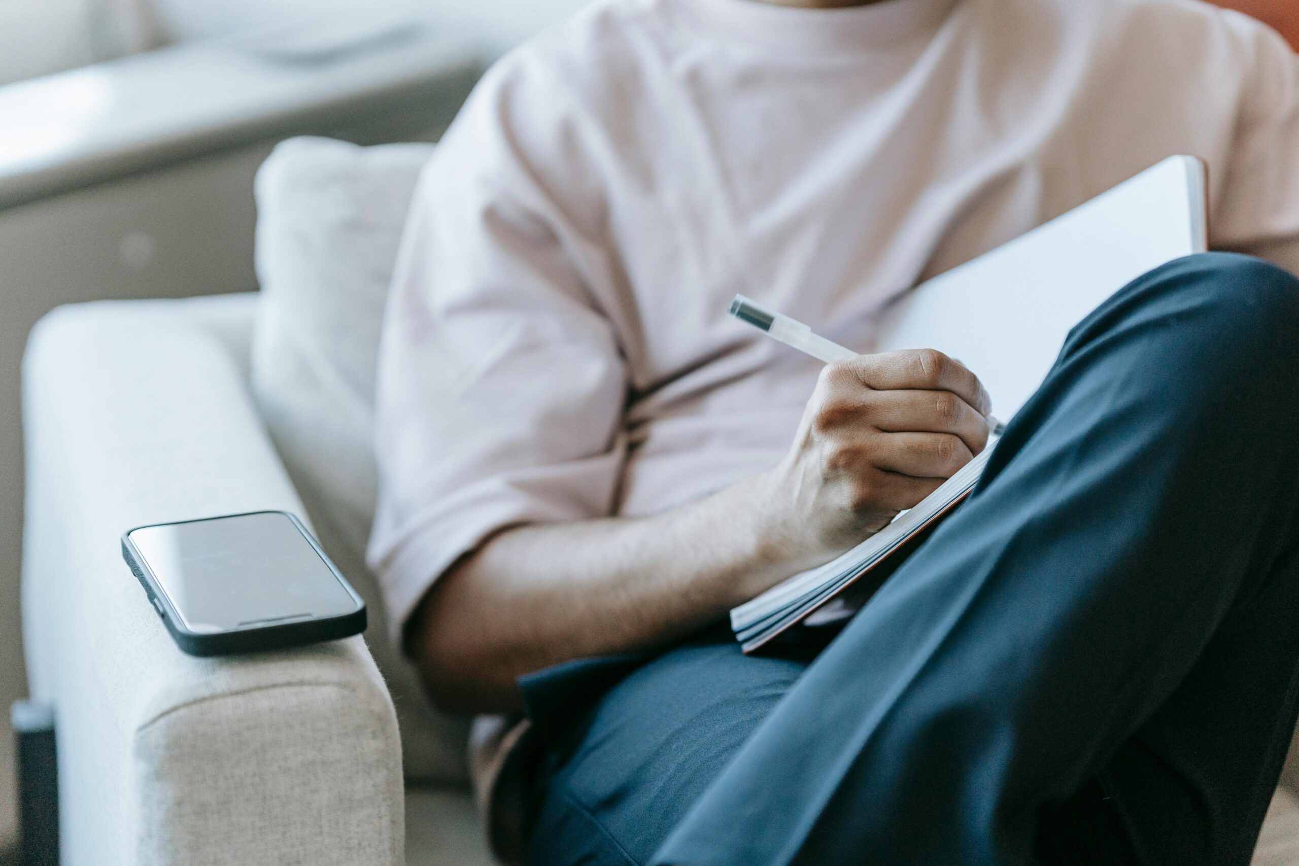 A person relaxes on a couch, writing in a notebook