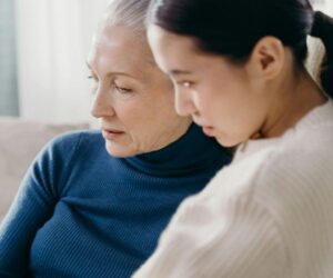 An older woman and a younger woman sit closely, sharing a quiet moment