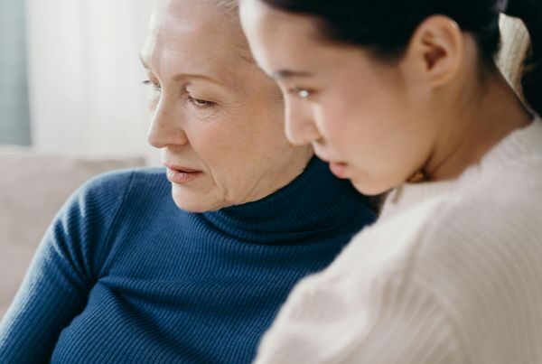 An older woman and a younger woman sit closely, sharing a quiet moment