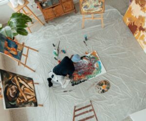 Artist painting on the floor surrounded by artworks