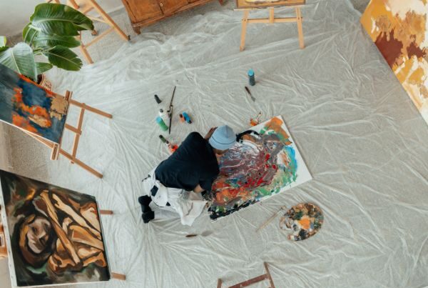 Artist painting on the floor surrounded by artworks