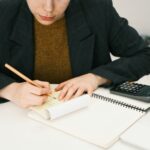 Person writing on a notepad at a desk with a calculator