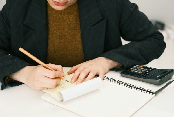 Person writing on a notepad at a desk with a calculator