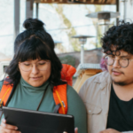 Two people siting on steps outside looking at a tablet.