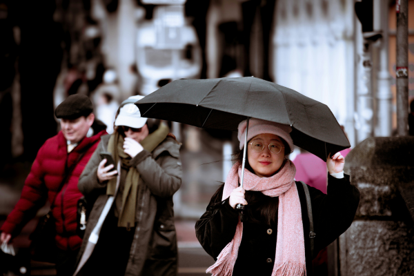 A woman with an umbrella walking outside in front of several other people.